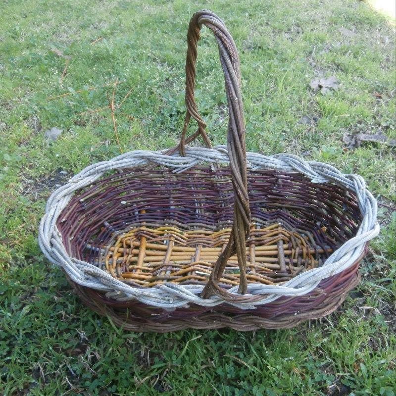 Un grande cesto ovale con manico intrecciato e bordo chiaro, sull'erba
